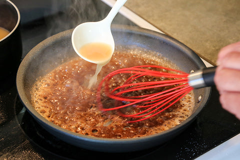 Image of a human hand holding a whisk as they make the brown gravy in the same pan that the steaks were fried in.