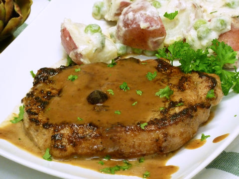 Image of plated pork loin steak with gravy and a side dish.