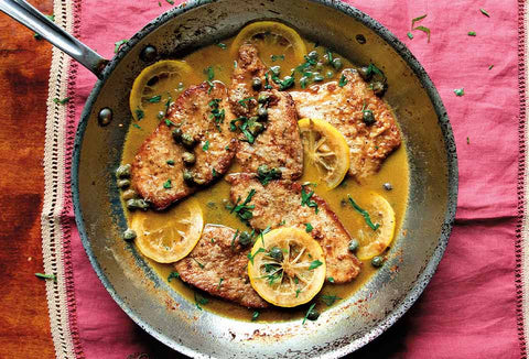 Image of veal cutlets in frying pan with lemon slices and capers.