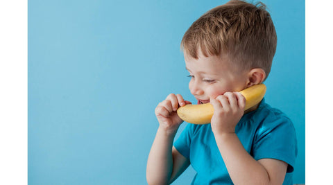 little boy in a turquoise shirt pretending to use a banana as a telephone
