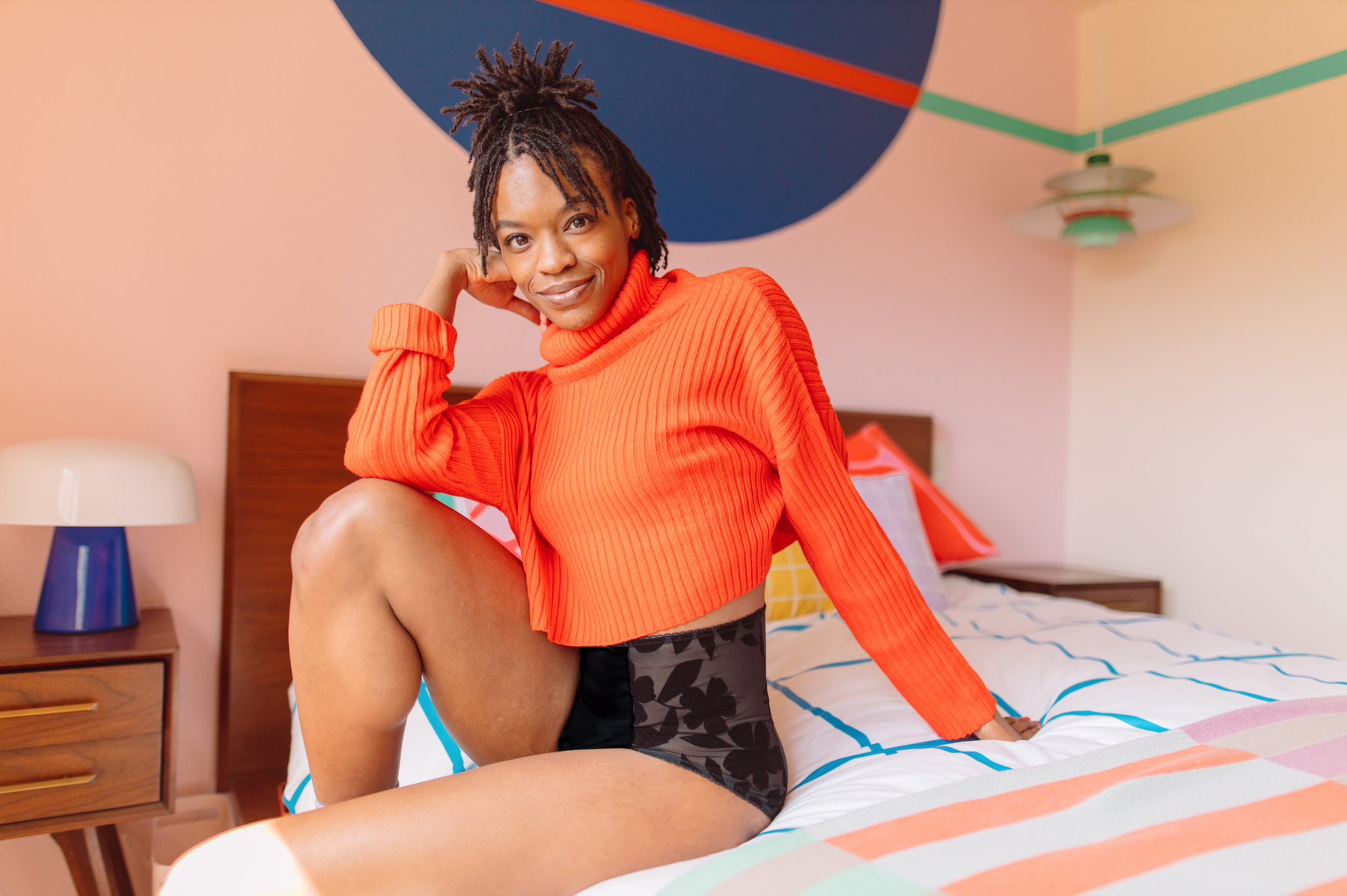 Woman sits on bed wearing Hello Period undies