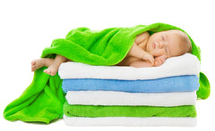 cute baby wrapped in a green towel. Sleeping on a stack of five folded towels