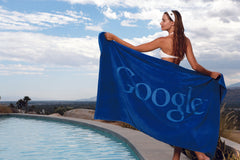 Bikini clad girl holding Google printed blue Towel by the swimming pool