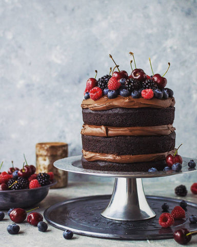 MY BAKER Top 25 Inspirational Baker Awards - @domestic_gothess - A delicious vegan chocolate cake on a cake stand with a beautiful backdrop
