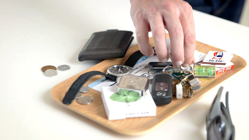 hand reaching to grab keys from a dish of everyday carry items – watches, coins, cards
