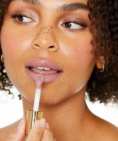 Model applying Lovingly Lip Tinted Lip Oil in shade b. sincere (a bare peach shade.)