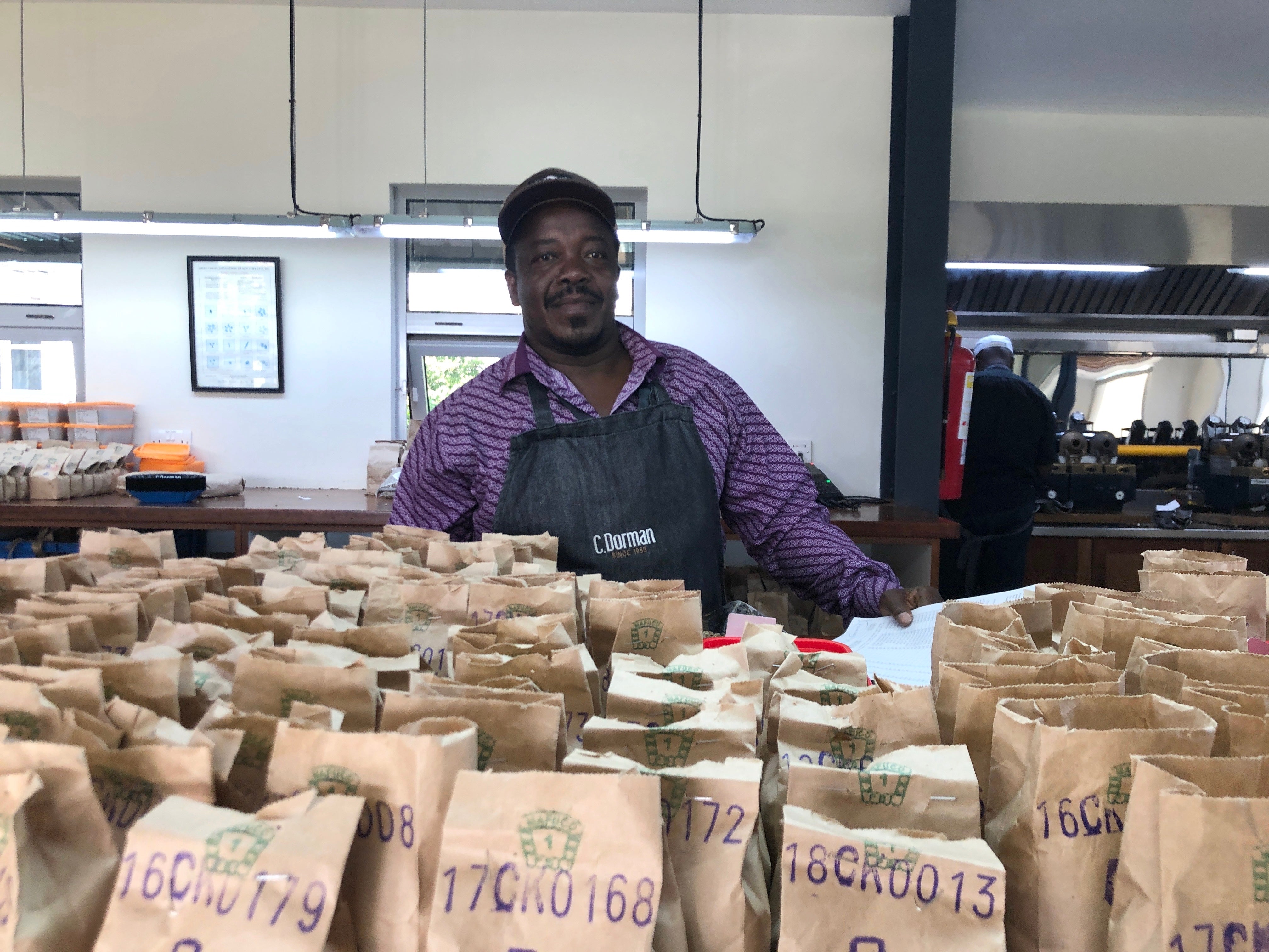 Man smiling at a table filled with coffee samples at Dormans cupping lab in Nairobi Kenya