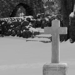 Cross on snow with stone wall and steps leading into a stone wall doorway.