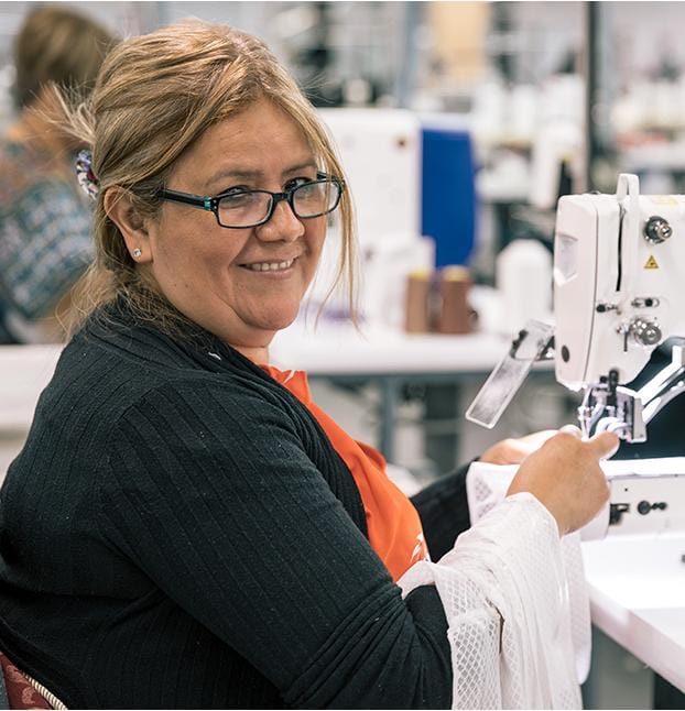 A photo of a woman sitting at a sewing machine with a smile on her face.
