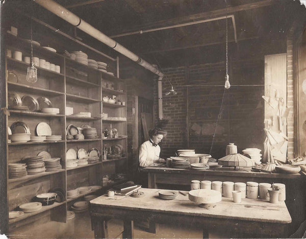 Mary Chase Perry with plates and lamps in studio. Historic photo post 1907.