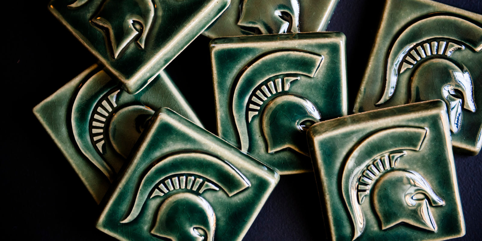 Our MSU Spartan Helmet tiles strewn across a black backdrop.