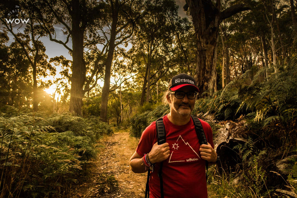 Sputnik walking down a trail, wearing a backpack, an ioMerino Outsider cap, and an ioMerino Universal Tee in Chilli with Mountain print