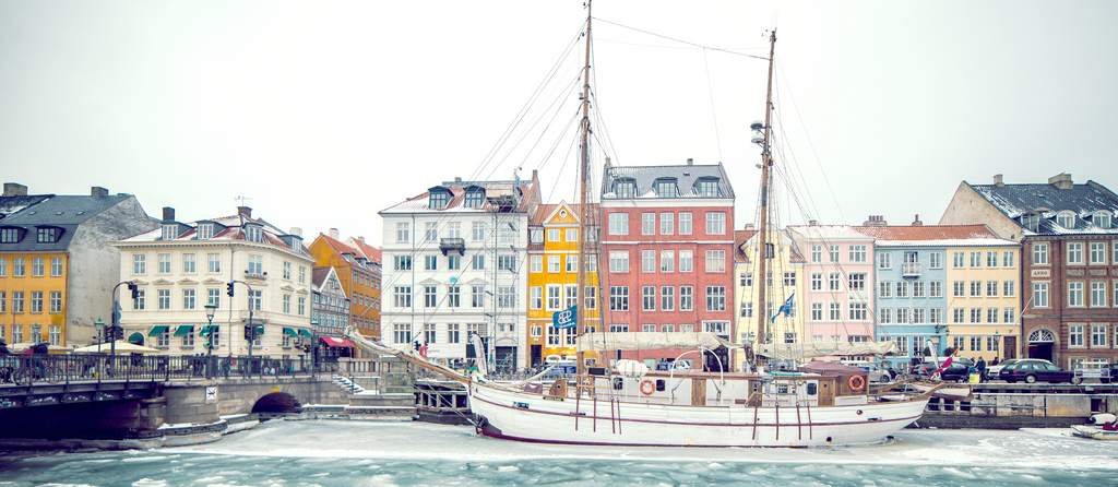 A wintry harbor scene with colorful buildings and a wooden ship in icy Copenhagen, Denmark.