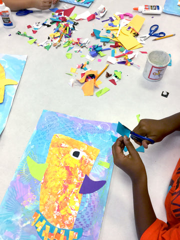 elementary student's hands working on a colorful and bright fish collage with mixed media