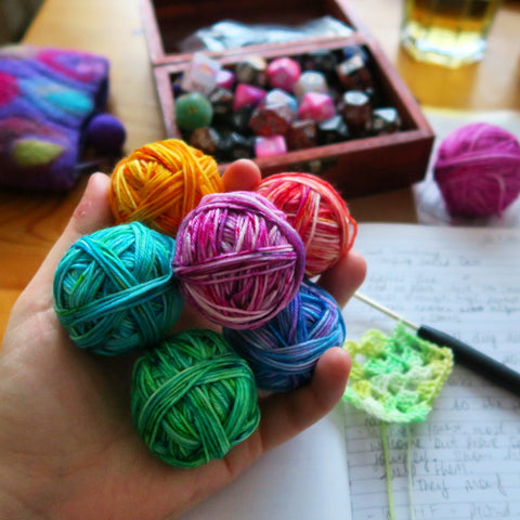 Brightly coloured mini skeins balled up, with a box of dice in the background