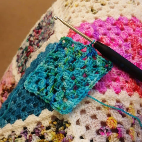 Turquoise granny square with colourful crochet blanket behind