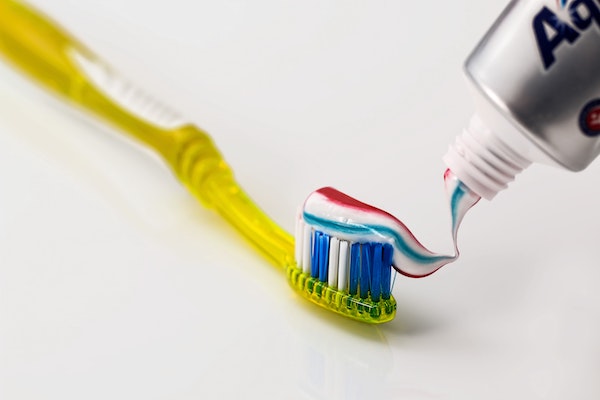 colorful toothpaste being applied to a yellow toothbrush