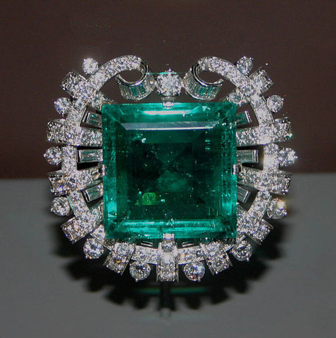 A beveled square-cut emerald in a platinum setting, surrounded by 109 round and 20 baguette cut diamonds.