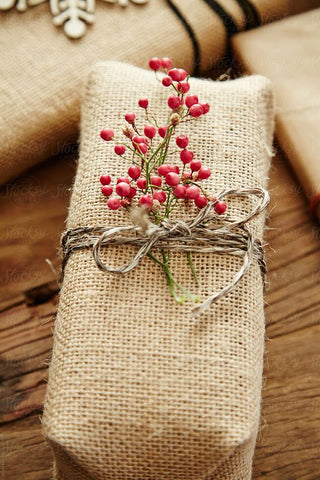 Rectangular package wrapped in burlap tied with twine and decorative red berries