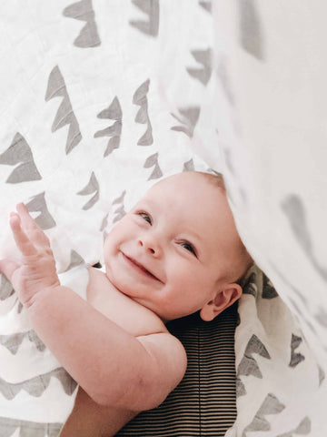 baby playing hide and seek under a swaddle blanket