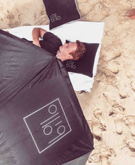 lying on sand with billo under head with billo umbrella