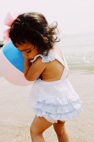 little girl at beach with beachball and ruffle playsuit