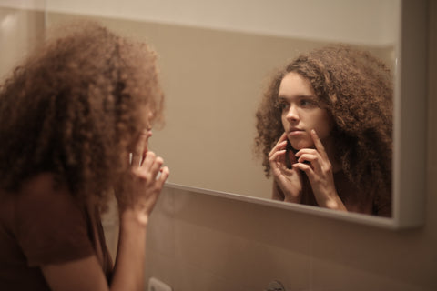 Woman looking stressed while looking at her skin in the mirror 