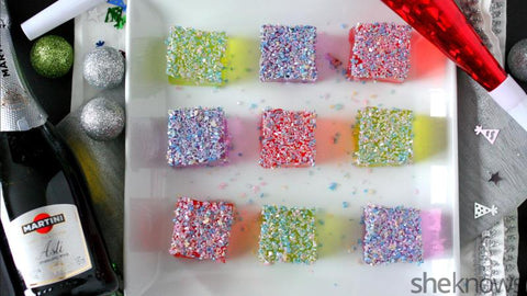 Champagne bottle next to three rows of colored and glittered jello squares