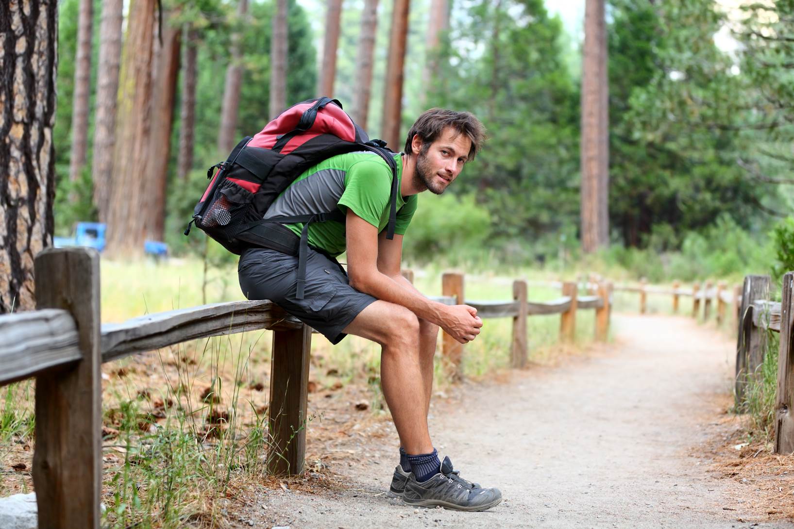  A hiker with a red backpack resting on a small fence  