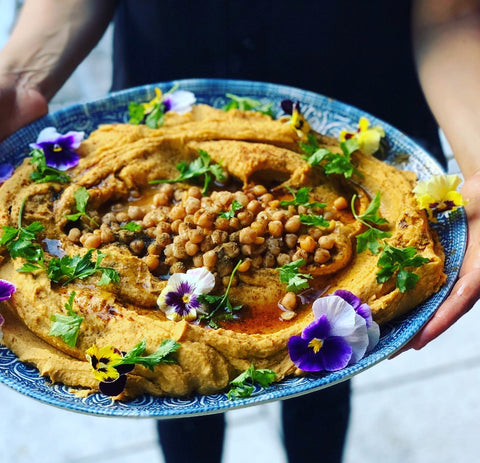 A large platter of hummus is held by two hands. 
