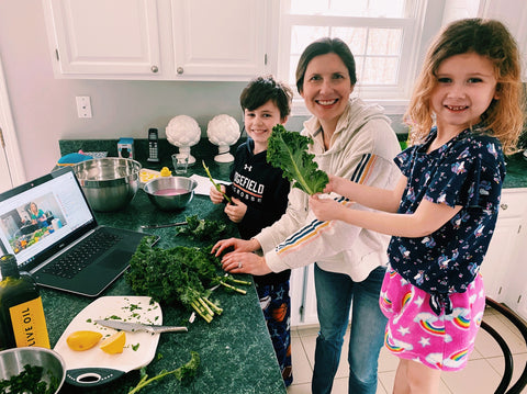 A mom cooking with her kids while watching a laptop