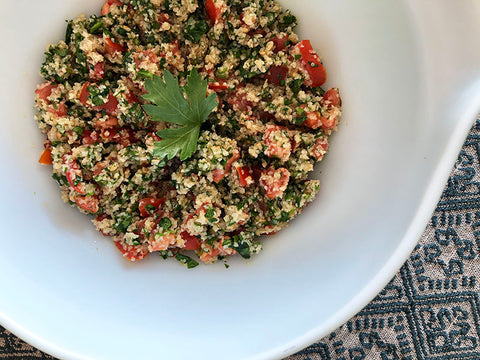 A white bowl holds tabbouleh, garnished with a sprig of parsley.