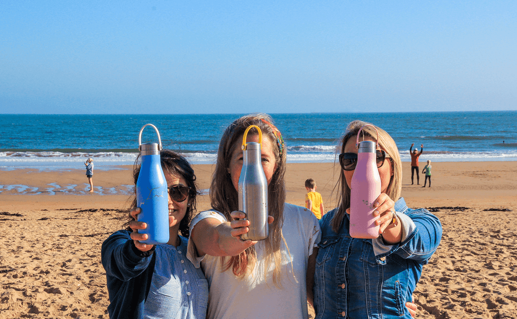 3 women on beach with reusable water bottles