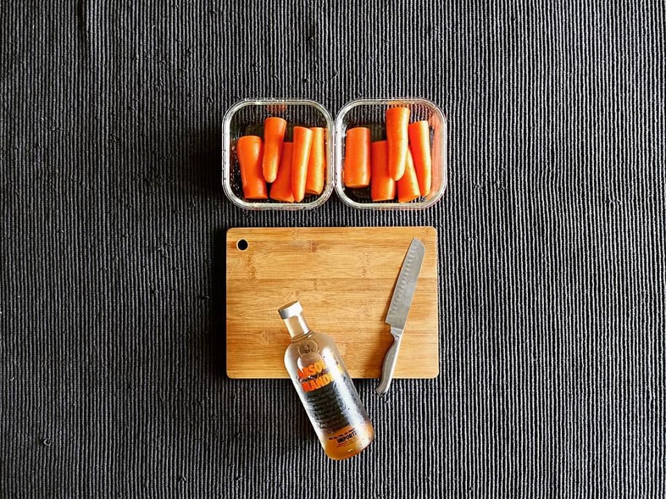 chopped-carrots-in-galss-containers-absolut-vodka-bottle-and-knife-on-wooden-bamboo-chopping-board
