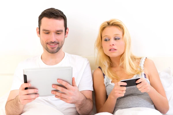 Couple playing with smartphones in bed