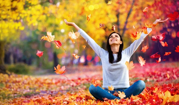 Young girl throwing up Autumn leaves in a field