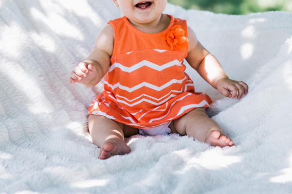 Close up of baby girl wearing an orange dress laughing on a white blanket.
