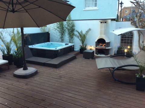 Mediterranean inspired hot tub set up with brown decking and a fire oven