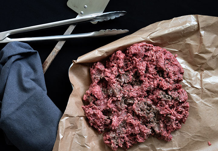 Ground beef on a metal sheet tray with salt and pepper.