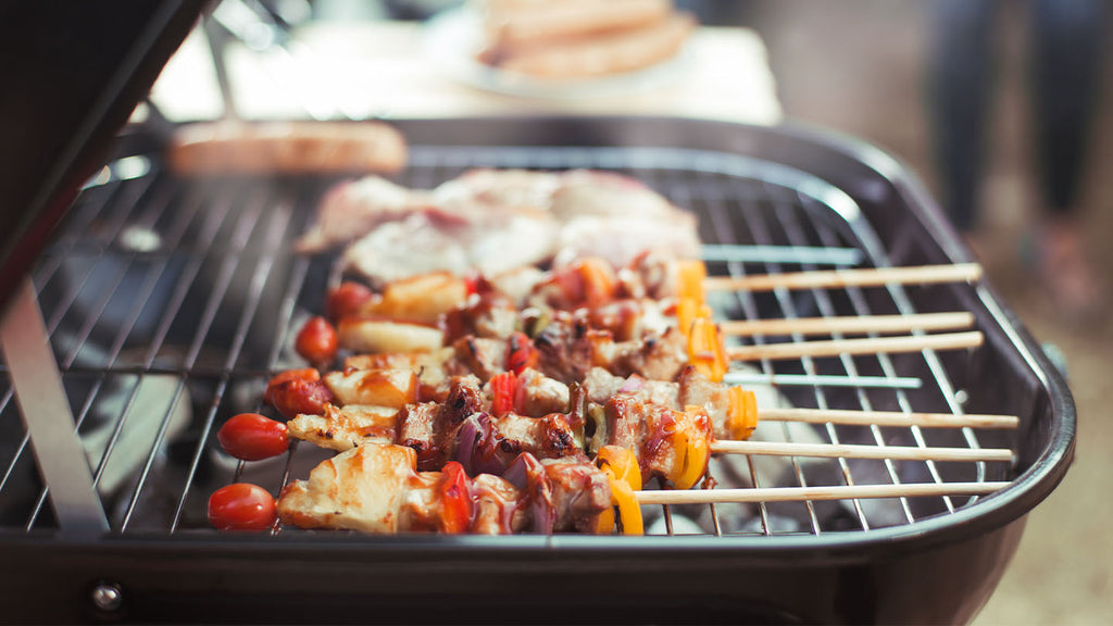 Veggie and chicken skewers cooking over a hardwood coal grill.