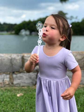 little girl in lavender twirl dress blowing bubbles