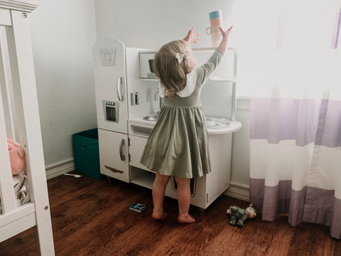 2 year old playing kitchen in her bedroom with a pretty green dress