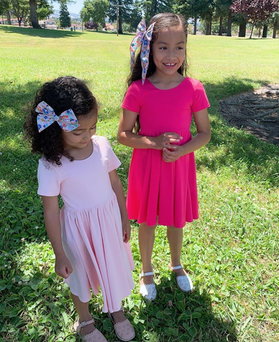 two little girls in pink twirl dresses playing on the grass outside