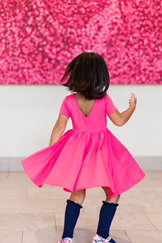 girl in bright pink dress and black kneehighs twirling in front of bright pink art installation