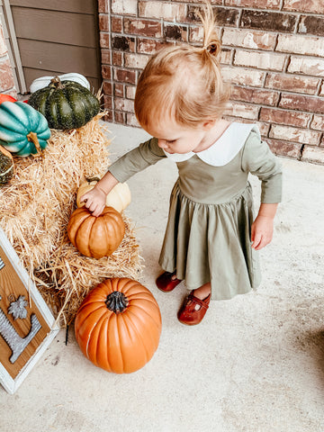 cute kid in green dress touching pumpkins on front porch
