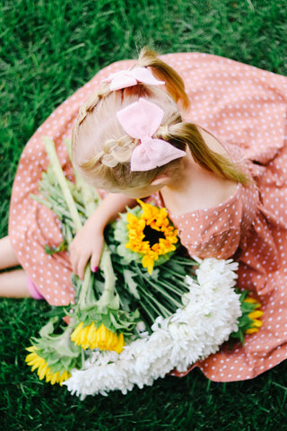 girl in twirl dress with braids and bow holding sunflowers