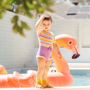 Cute baby girl by pool in rainbow coloured romper
