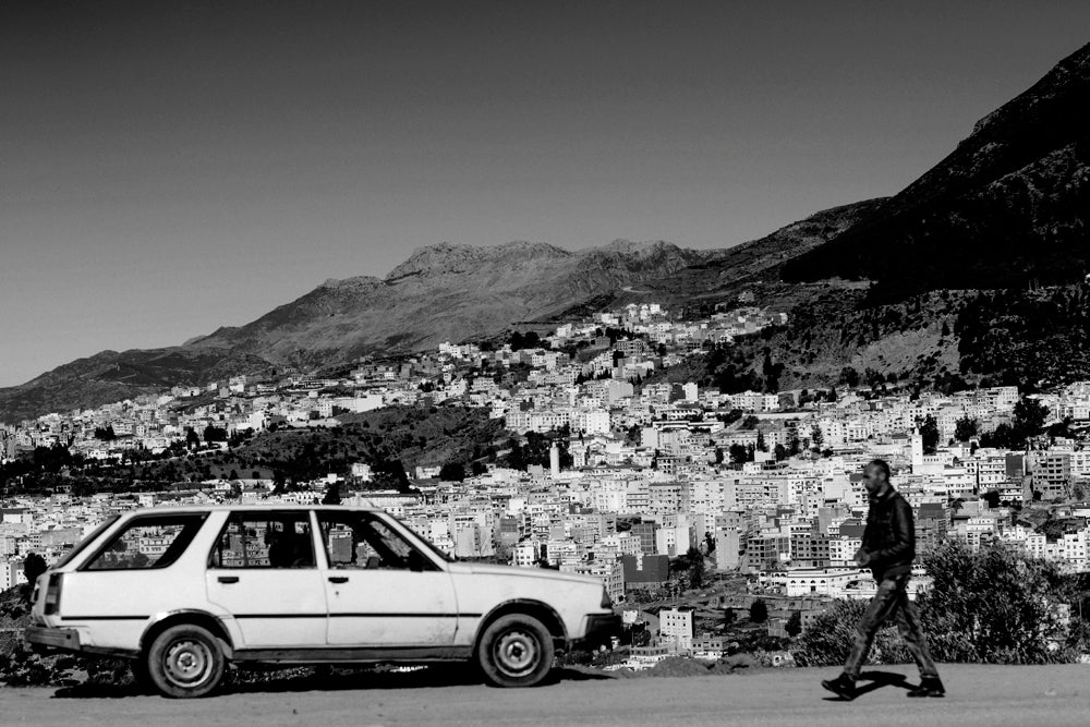 A man walks along the outskirts of Chefchaouen, Morocco with the city behind him.