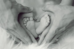 New baby image of parents hands and baby feet in black and white.