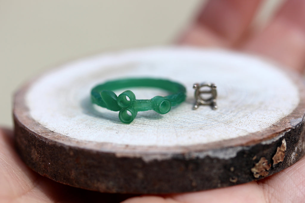 Wax carving of clients custom made ring with stone setting set beside it 